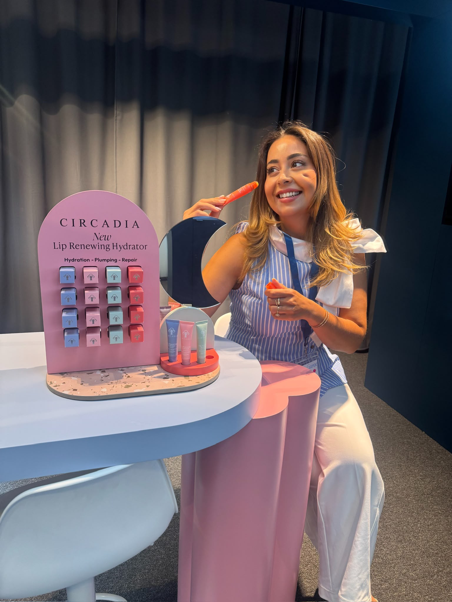 Kosmetikerin Gamze Marasli an einem Circadia-Messestand, sie testet lächelnd den Lip Renewing Hydrator vor einem Produktdisplay